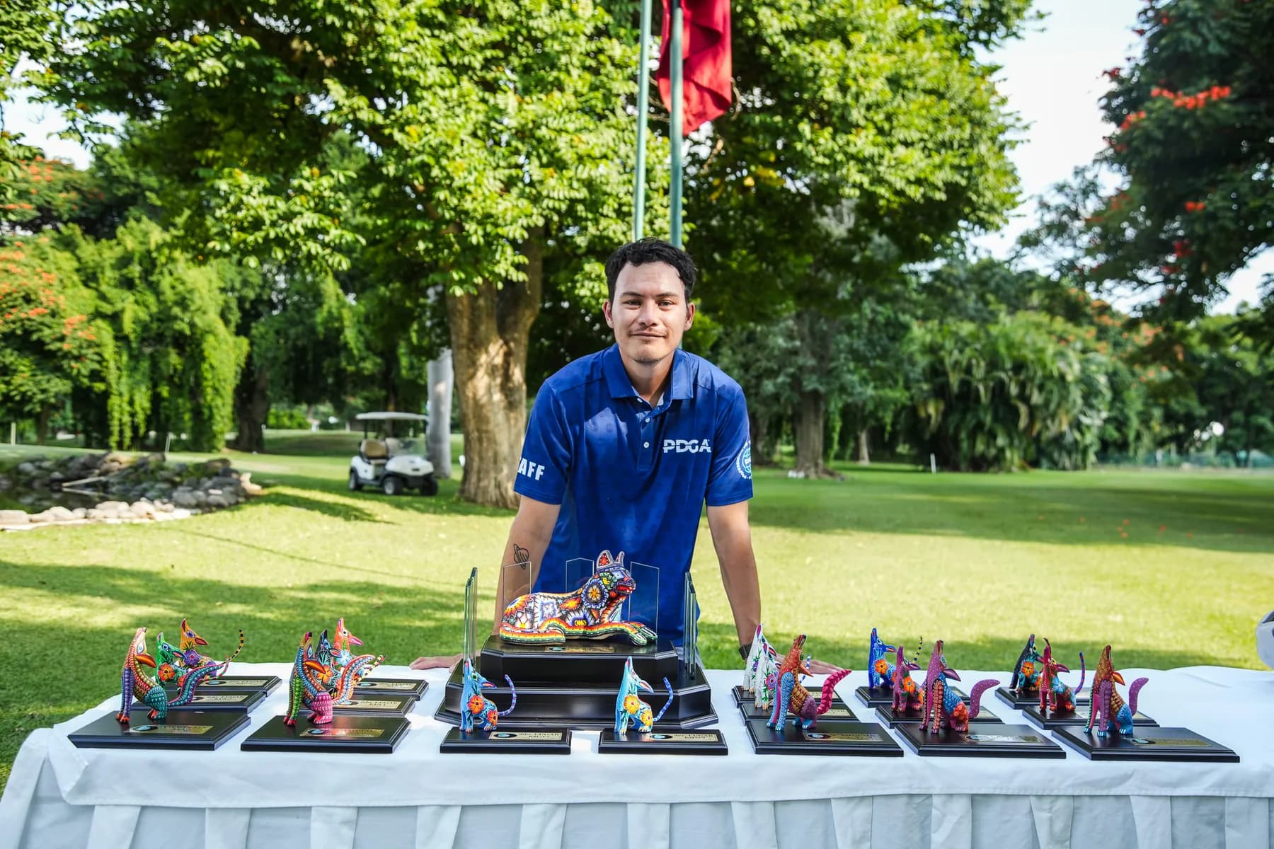 Fabián Oloarte in a blue PDGA shirt behind a table of colorful tournament awards.