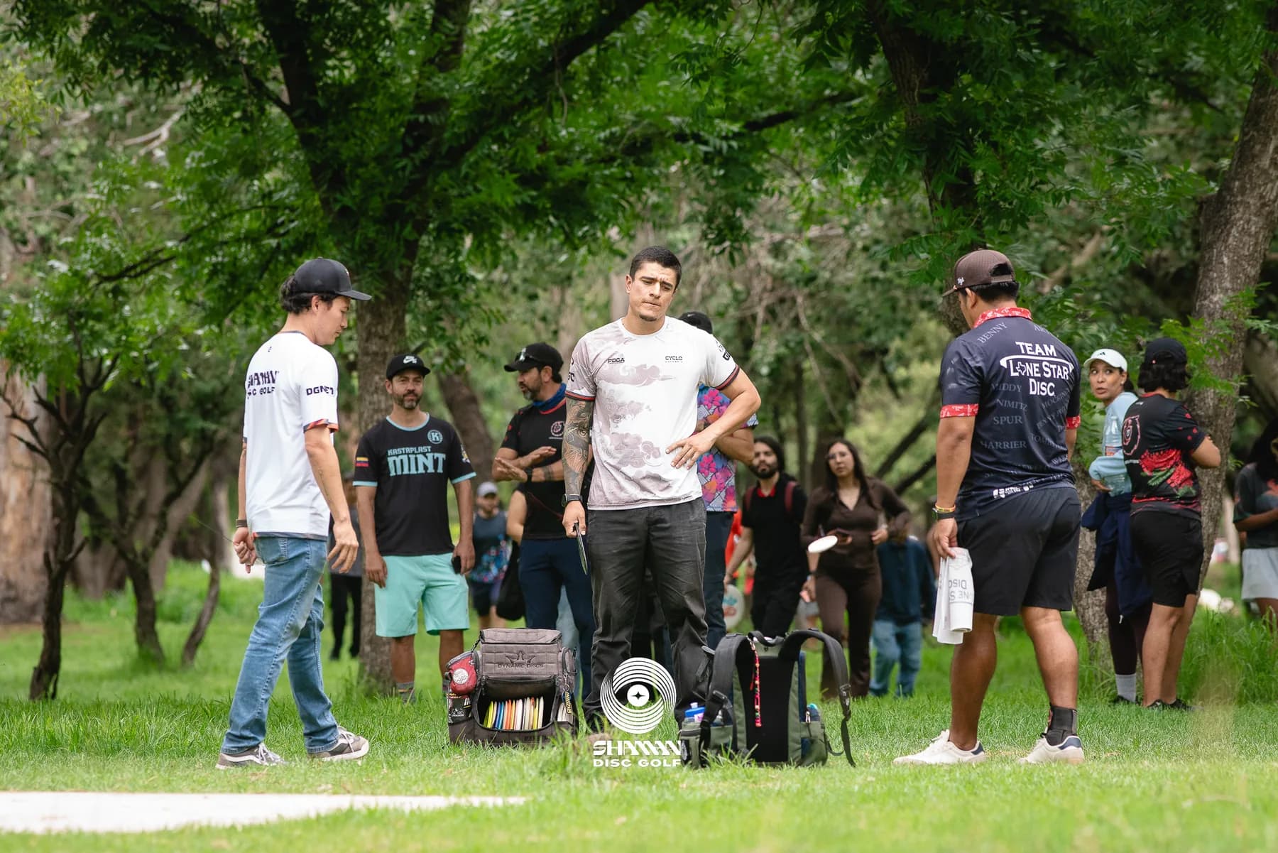 Fabián Oloarte holding a disc while directing a tournament group in a wooded park.